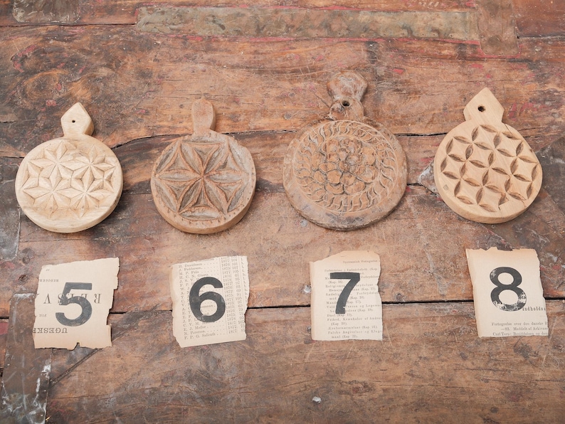 May include: Four round, wooden, decorative cutting boards with carved floral and geometric designs. Each board has a handle. Below the boards are four torn pieces of paper with the numbers 5, 6, 7, and 8 printed on them.