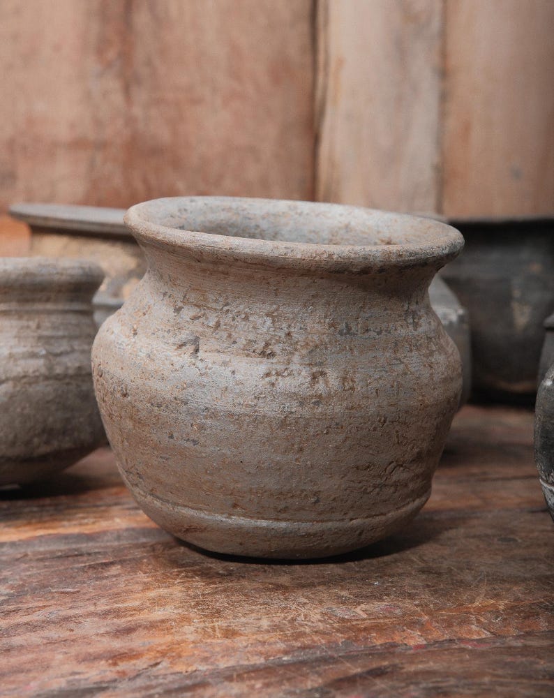 Peut inclure: Plusieurs petits pots en poterie beige, d'aspect vieilli. Les pots ont un corps arrondi et un bord large l&eacute;g&egrave;rement &eacute;vas&eacute;. La surface de la poterie pr&eacute;sente un aspect textur&eacute;. D'autres pots similaires et une surface en bois sont en arri&egrave;re-plan.