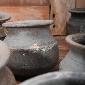 Peut inclure: Plusieurs petits pots en c&eacute;ramique grise, de forme arrondie et &agrave; bord &eacute;vas&eacute;. Les pots ont une surface textur&eacute;e et pr&eacute;sentent des signes d'usure, avec des zones de peinture &eacute;caill&eacute;e. L'arri&egrave;re-plan est une surface en bois chaleureuse.