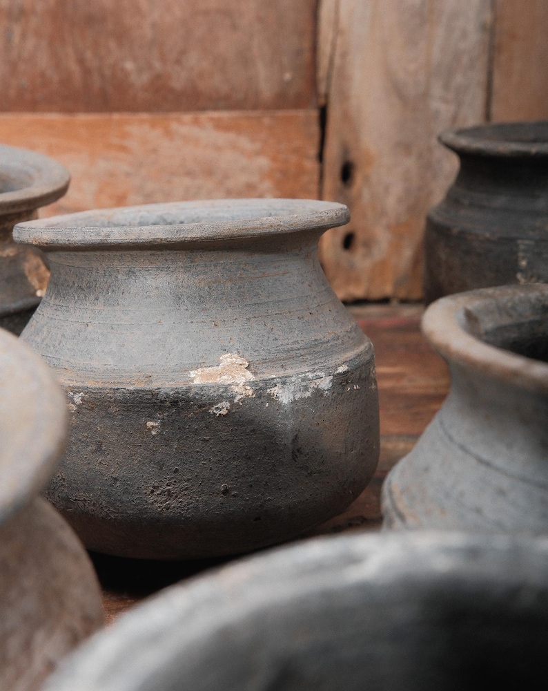 Peut inclure: Plusieurs petits pots en c&eacute;ramique grise, de forme arrondie et &agrave; bord &eacute;vas&eacute;. Les pots ont une surface textur&eacute;e et pr&eacute;sentent des signes d'usure, avec des zones de peinture &eacute;caill&eacute;e. L'arri&egrave;re-plan est une surface en bois chaleureuse.