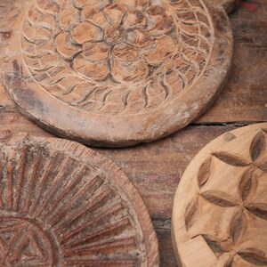 May include: Close-up of several antique wooden serving boards with carved floral and geometric designs. The boards are various sizes and shapes, with a rustic, weathered appearance. The wood has a warm, brown tone.