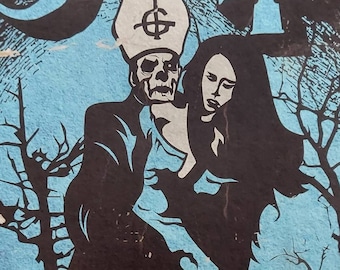May include: A black and white illustration of a figure in a bishop's hat and robe holding a woman in a long dress. The figure has a skull face and a symbol on the hat. The background is blue with trees and flames. The text "STAND BY HIM" is at the bottom of the image.
