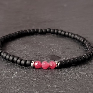 Peut inclure: Un bracelet en perles noires avec trois perles de pierres précieuses roses.