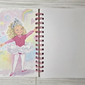 May include: A spiral-bound notebook with a colorful illustration of a young girl in a pink leotard and tutu, with a crown, surrounded by hearts, butterflies, and rainbows. The notebook has a blank page next to the illustration.