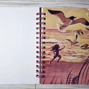 May include: A spiral-bound notebook with a blank white page and a colorful illustration. The illustration depicts a child running on a beach with seagulls flying overhead. The artwork is in shades of brown, orange, and yellow.
