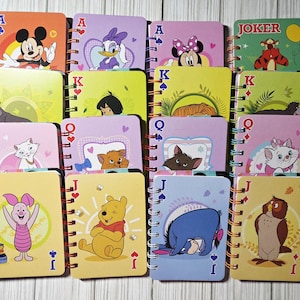 May include: A collection of colorful, spiral-bound notebooks featuring Disney characters and playing card suits. Each notebook cover displays a different character, including Mickey Mouse, Winnie the Pooh, and Marie the cat, with card symbols like hearts and spades.