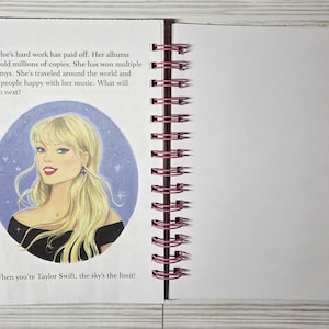 May include: Open notebook with a spiral binding and blank pages. The left page features an illustration of a blonde woman in a black top, with text about her achievements. The text reads, "When you're Taylor Swift, the sky's the limit!"