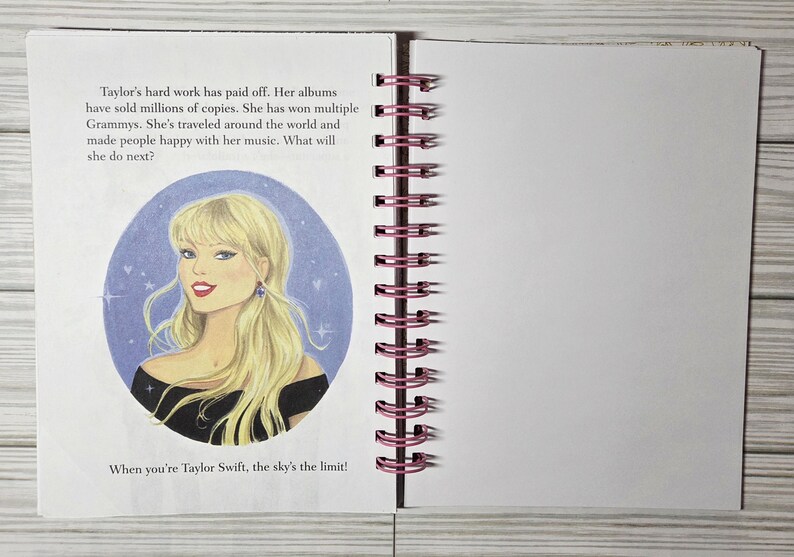May include: Open notebook with a spiral binding and blank pages. The left page features an illustration of a blonde woman in a black top, with text about her achievements. The text reads, "When you're Taylor Swift, the sky's the limit!"