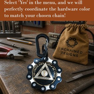 May include: A circular medallion featuring a black and silver bicycle chain outer ring surrounding a central triangle emblem. The emblem displays the text TO THINE OWN SELF BE TRUE, UNITY, SERVICE, RECOVERY, and the Roman numeral V. A black carabiner is attached.