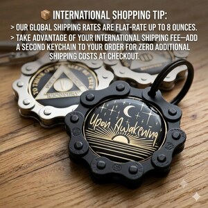May include: A black circular keychain featuring a gear-like metal frame and a central graphic of a crescent moon, stars, and a rising sun with the text Upon Awakening. A second silver keychain with a triangular emblem is visible in the background.