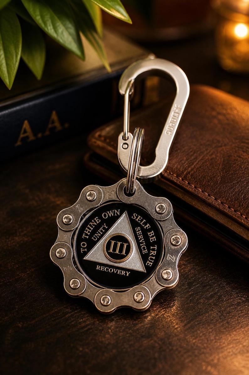 May include: A silver-toned metal keychain featuring a circular gear-like outer frame and a central black medallion. The medallion displays a silver triangle with the Roman numeral III, surrounded by the text TO THINE OWN SELF BE TRUE.