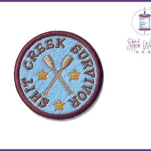Op de afbeelding: Een geborduurde patch in bruin en blauw met de tekst "Creek Survivor" en twee gekruiste peddels. De patch heeft een donkerrode rand en vier gouden sterren.