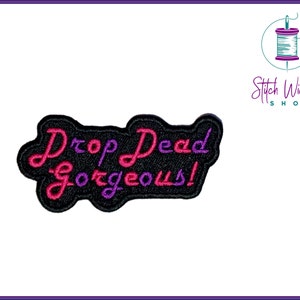 Peut inclure: Patch brodé noir avec le texte "Drop Dead Gorgeous!" en lettres roses et violettes.