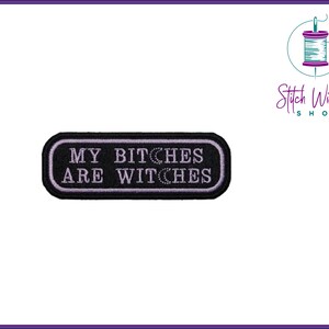 Puede incluir: Parche bordado en blanco y negro con costuras moradas. El parche dice "My Bitches Are Witches".