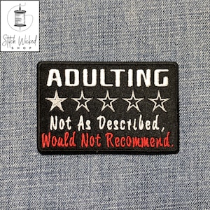 Peut inclure: Un écusson brodé noir avec le mot "ADULTING" en blanc, au-dessus de cinq étoiles blanches. En dessous, le texte se lit "Not As Described, Would Not Recommend" en blanc et rouge. L'écusson est rectangulaire.