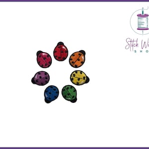 Puede incluir: Un conjunto de siete parches de mariquita de colores arcoíris para planchar. Los parches están dispuestos en círculo.