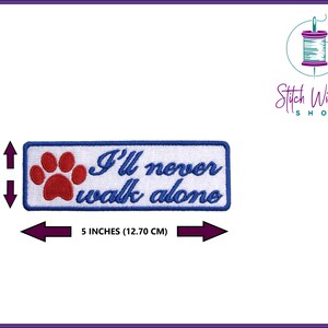 May include: White embroidered patch with blue border and red paw print. The text "I'll never walk alone" is embroidered in blue.