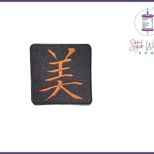 May include: A black fabric patch with an orange embroidered Japanese character, "美" (pronounced "bi"), meaning "beauty".