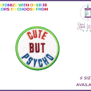 Peut inclure: Un patch rond brodé blanc avec une bordure verte. Le texte "CUTE BUT PSYCHO" est brodé en couleurs arc-en-ciel.