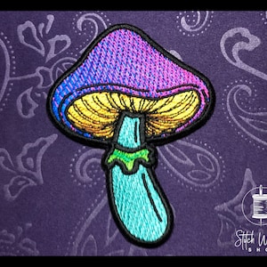 Może przedstawiać: Kolorowa haftowana łatka w kształcie grzyba w schemacie kolorystycznym fioletowym, niebieskim, żółtym i zielonym. Grzyb ma zaokrąglony kapelusz i długą, smukłą nóżkę.