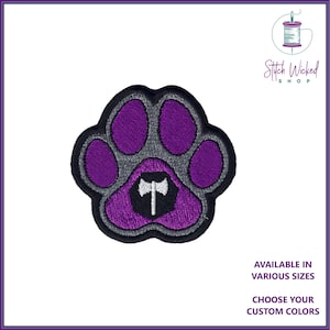 Peut inclure: Patch brodé en forme de patte d'animal, de couleur violette et grise, avec un symbole de hache blanc et gris au centre. Le texte "Stitch Wicked Shop" est dans le coin supérieur droit de l'image.