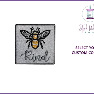 May include: Embroidered iron-on patch featuring a bee and the word "Kind" on a grey background. The bee is black with yellow stripes.