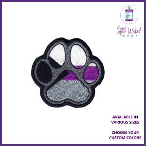 Op de afbeelding: Een geborduurde patch in de vorm van een poot, met grijze, zwarte, witte en paarse strepen. De tekst "Stitch Wicked Shop" staat in de rechterbovenhoek van de afbeelding.