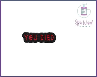 Puede incluir: Parche bordado negro con el texto "YOU DIED" en rojo.