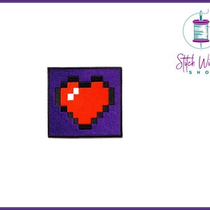May include: A purple felt patch with a red pixelated heart on it. The patch is square shaped and has black stitching around the edges.