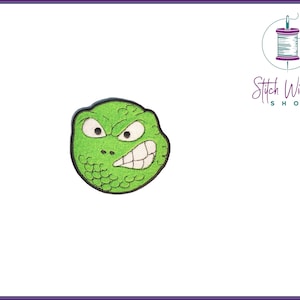 Pode incluir: Etiqueta de feltro verde para passar a ferro com uma cara de desenho animado com uma expressão de zangada e dentes afiados.