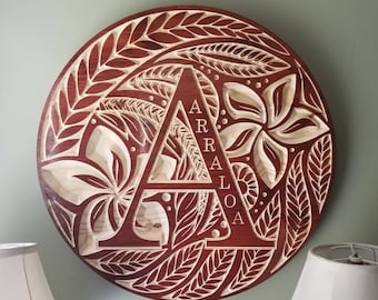 May include: A wooden round plaque with a carved floral design and the letter "A" in the center. The letter "A" is surrounded by leaves and flowers. The text "ARRALOA" is carved vertically inside the letter "A".