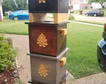 May include: Four wooden boxes stacked on top of each other. Each box has a carved floral design on the front and a wooden latch on the side. The boxes are stained in different shades of brown, gray, and black.