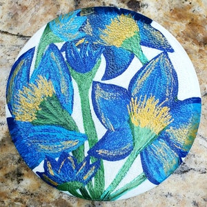 May include: A round ceramic plate with a white background and a blue and gold floral design. The flowers are stylized and have a textured appearance.