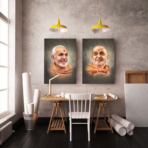 May include: Two framed portraits of a man with a white beard and orange robes hang on a gray wall. A wooden desk with a white chair, a lamp, and rolled paper sits in front of the portraits. Yellow pendant lights hang above.