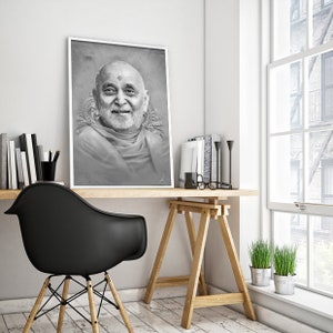 May include: A black and white portrait of a man with a beard and a white turban, hanging on a white wall above a wooden desk with a black chair and a wooden easel.