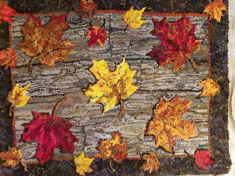 May include: A rug with a design of autumn leaves in shades of red, yellow, and orange on a gray background. The leaves are arranged in a random pattern and appear to be falling from a tree.