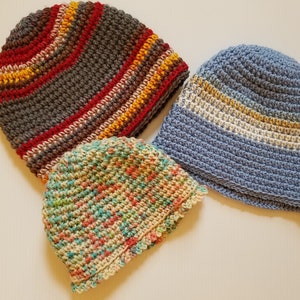 May include: Three crocheted hats in different colors and patterns. One hat is gray with red and yellow stripes, another is blue with white stripes, and the third is a multi-colored speckled pattern.