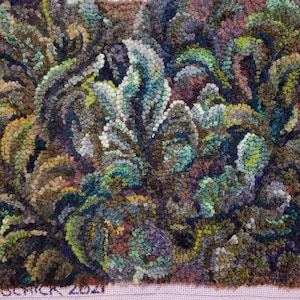 May include: A close-up of a rug hooking with a floral design. The rug is made of various shades of green, blue, brown, and yellow wool. The rug is signed "Veronica Oct 2021".