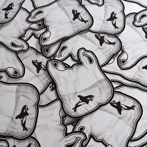 May include: A pile of black and white stickers with a graphic of a plastic bag and an orca whale. The stickers are printed on a white background.