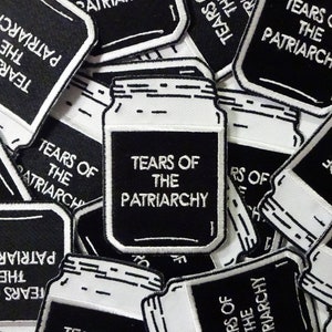 Peut inclure: Gros plan sur plusieurs patchs brodés en noir et blanc avec le texte "Tears of the Patriarchy" et un motif de pot.