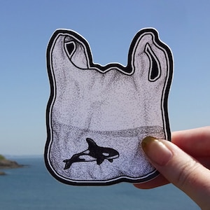 May include: A black and white illustration of a plastic bag with a small orca whale inside. The bag is drawn in a cartoon style and has a white background.