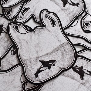 May include: A stack of black and white stickers with a graphic of an orca whale inside a plastic bag. The stickers are printed with a stippled pattern.