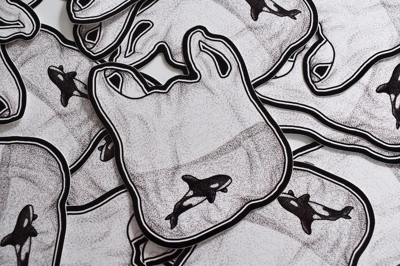 May include: A stack of black and white stickers with a graphic of an orca whale inside a plastic bag. The stickers are printed with a stippled pattern.