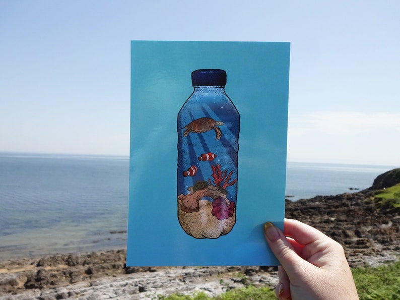 May include: A blue plastic bottle with a sea turtle, coral, and clownfish inside. The bottle is on a blue background. The image is a reminder of the impact of plastic pollution on marine life.