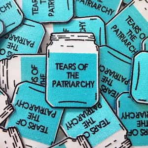 May include: A close-up of several blue and white fabric patches with the text "Tears of the Patriarchy" and a drawing of a mason jar.