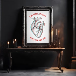 Könnte beinhalten: Ein gerahmter Druck mit einer detaillierten Illustration eines menschlichen Herzens in Rot und Blau mit 3D-Effekt. Der Text lautet "THIS HEART, IT BEATS BEATS FOR ONLY YOU" in Rot. Der Druck befindet sich auf einem dunklen Holztisch mit Kerzen.