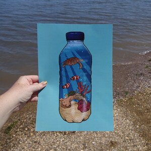 May include: A blue plastic bottle with a sea turtle, coral, and fish inside. The bottle is on a blue background.