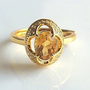 Könnte beinhalten: Ein goldener Ring mit einem großen ovalen Topas-Edelstein, der von kleineren, klaren Edelsteinen umgeben ist.