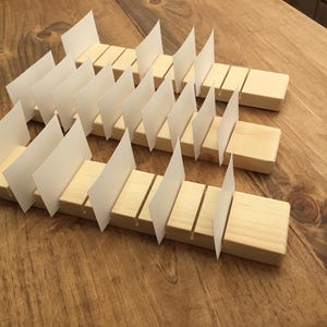 May include: Wooden card holder with slots for displaying cards. The holder is made of natural wood and has a rustic look. It is a great way to display business cards, greeting cards, or other small items.