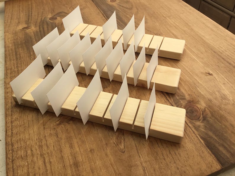 May include: Wooden card holder with slots for displaying cards. The holder is made of natural wood and has a rustic look. It is a great way to display business cards, greeting cards, or other small items.
